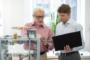 senior engineer telling measurements from caliper to his young intern while the man holding a laptop and being ready to put them down